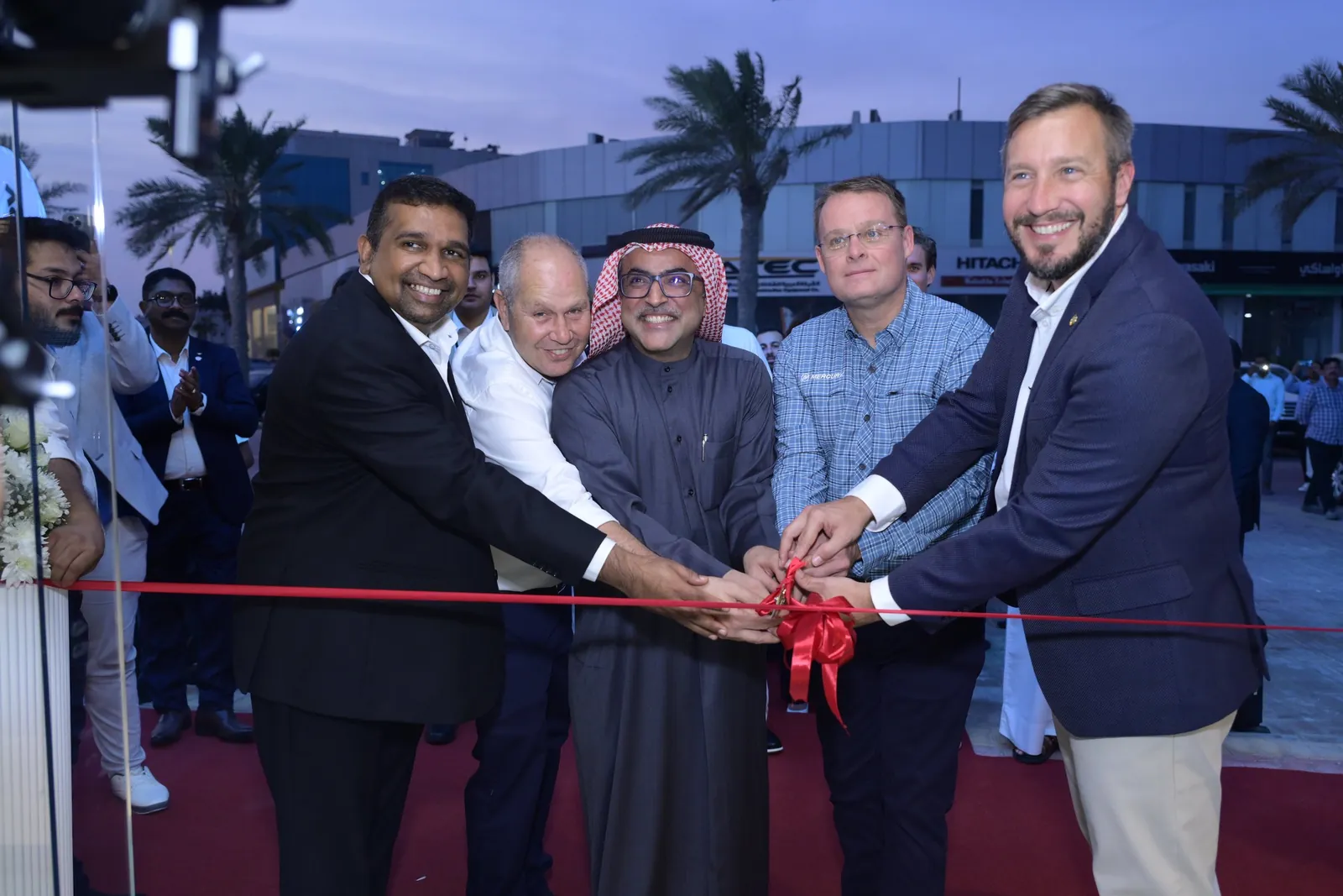 Five smiling executives cut the ribbon together at dusk