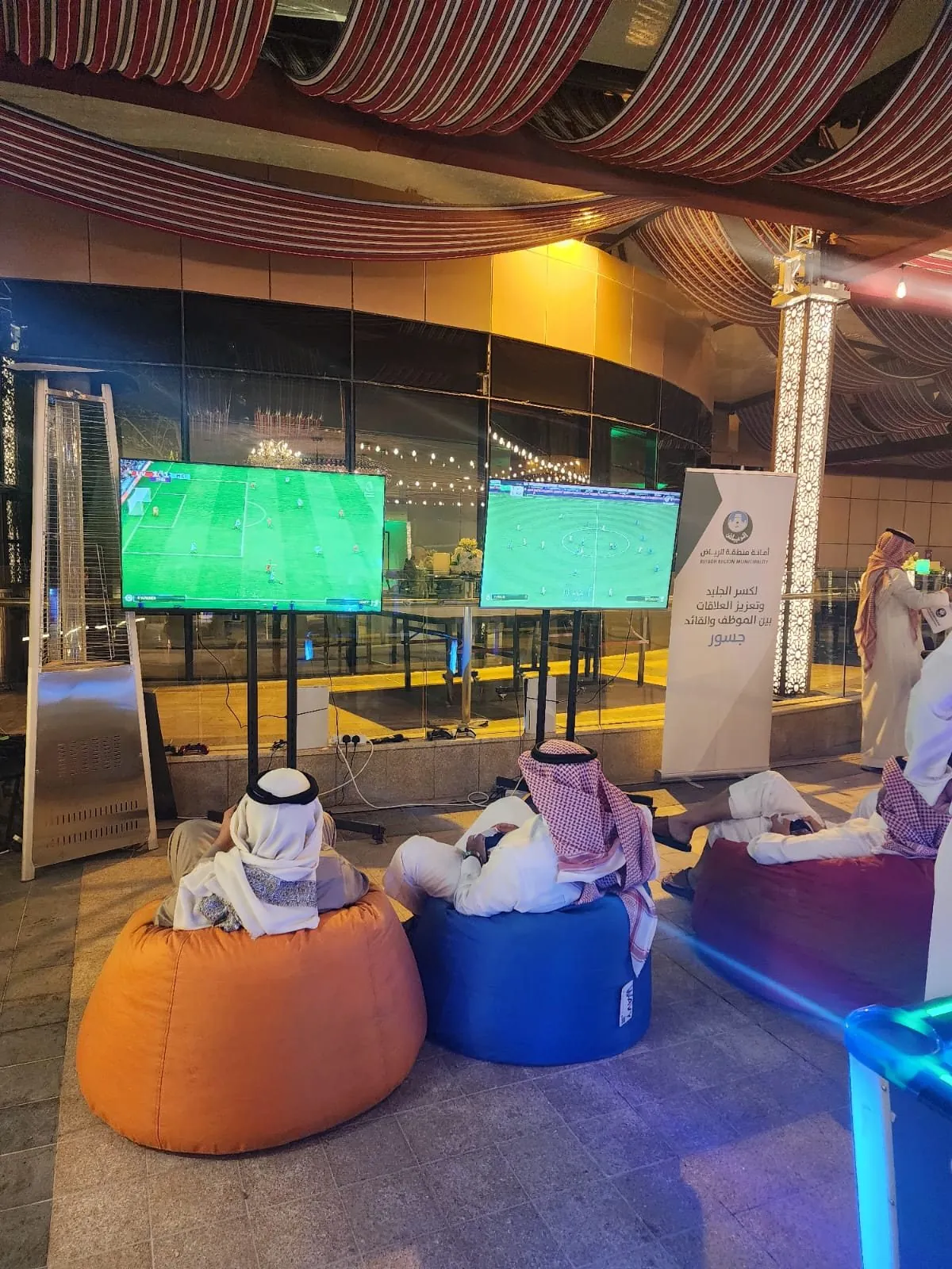 Guests on bean bags playing console football under Riyadh Municipality Josour banner