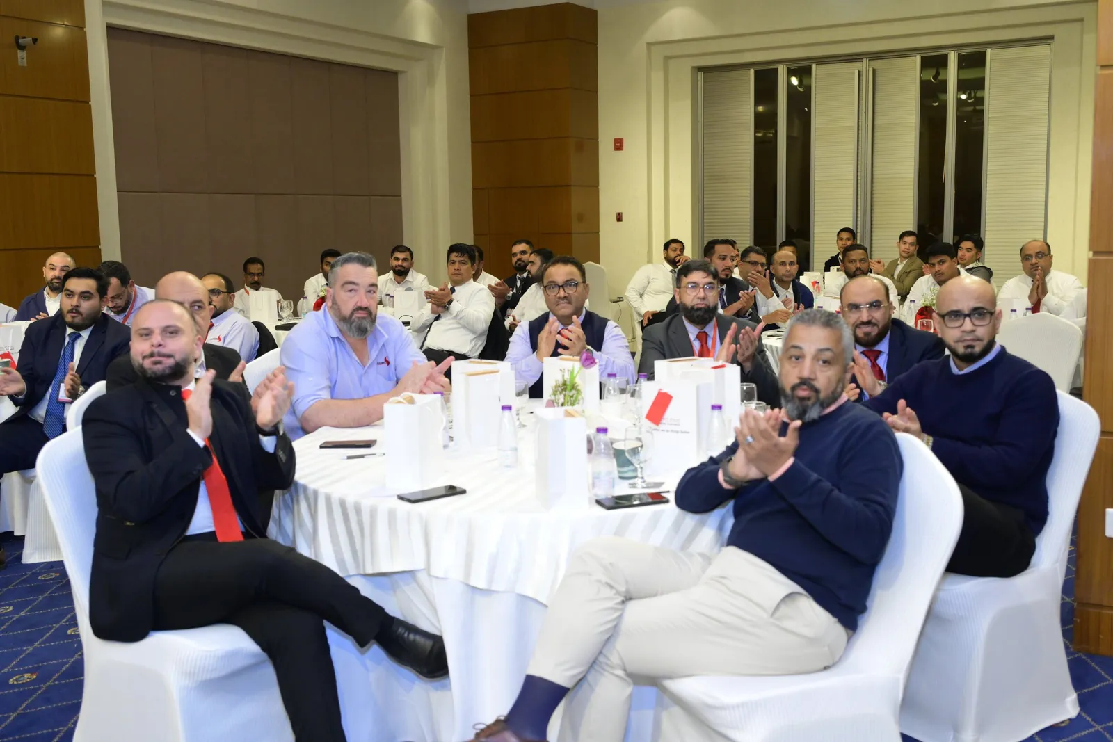 Employees at an end-of-year gathering clapping and smiling at their tables