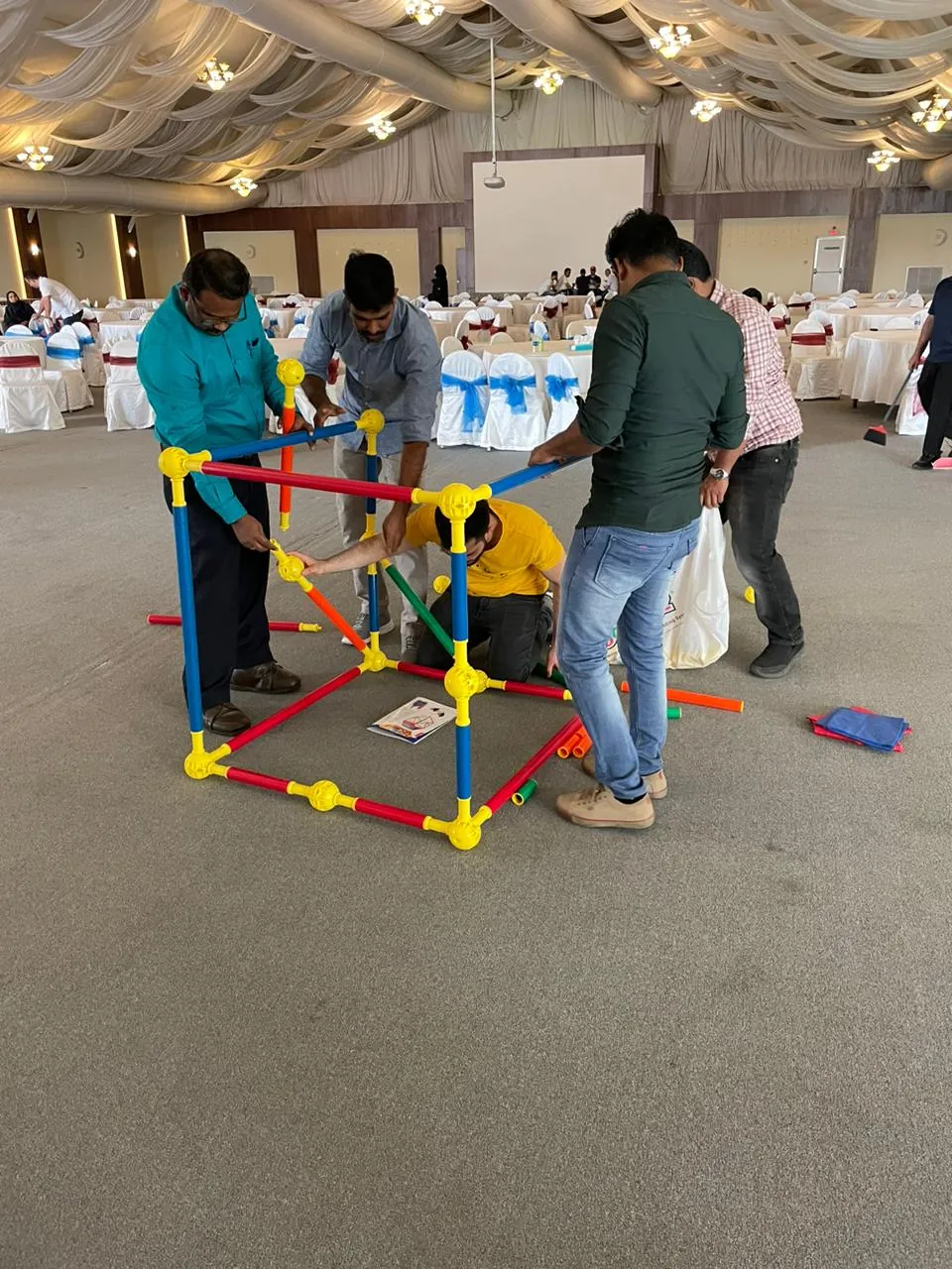 Team assembling a large geometric frame from coloured poles in a ballroom team building challenge