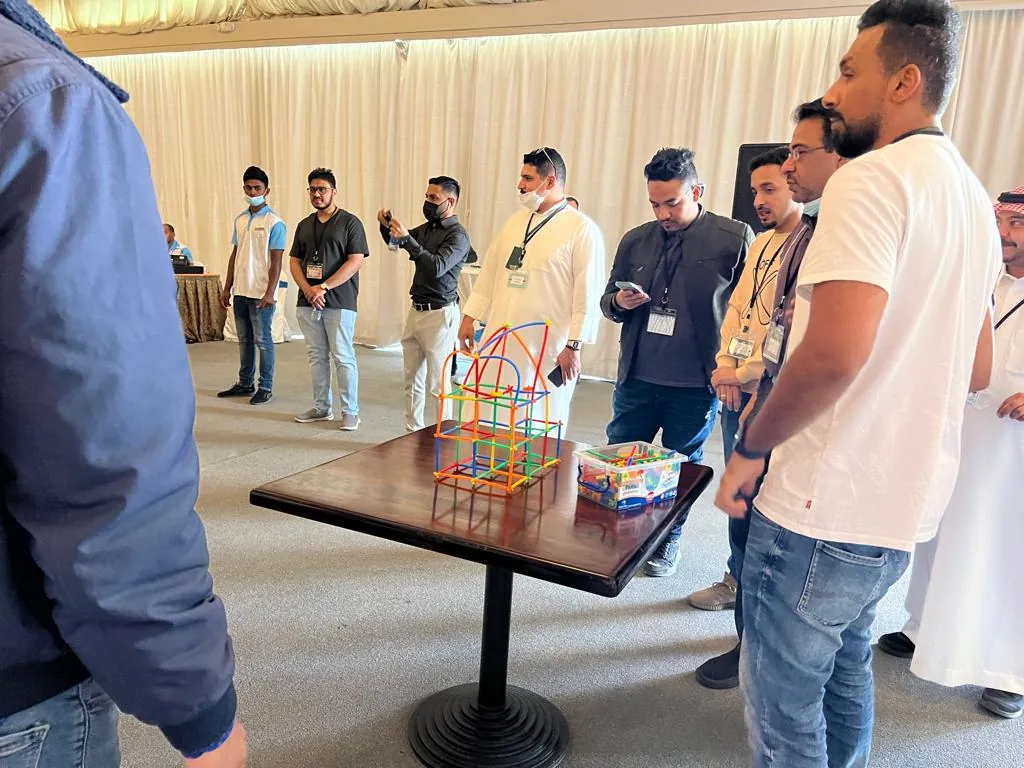 Colleagues gathered around a table watching a team's construction build during an indoor team building programme