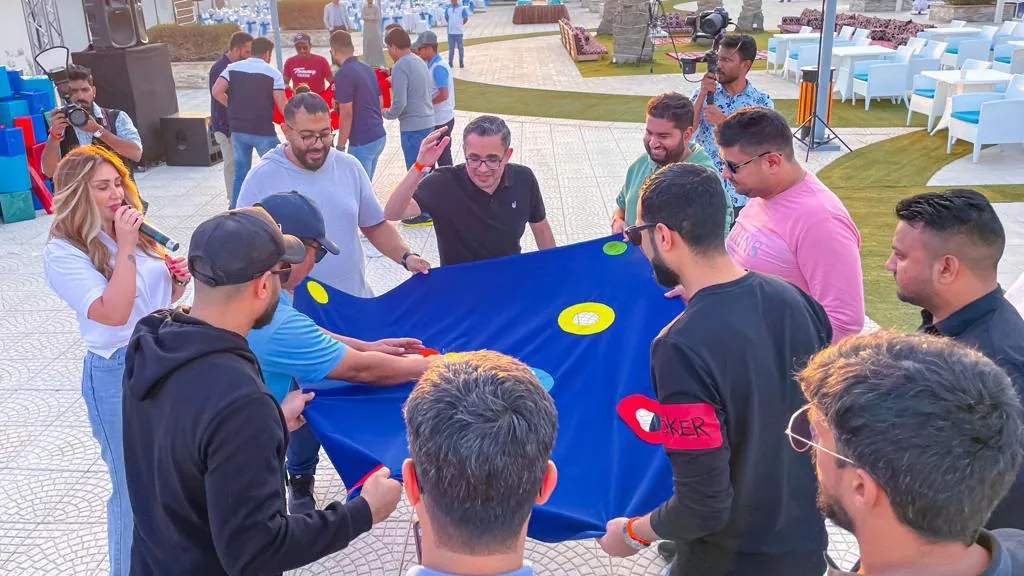 Group holding a large blue sheet to launch a ball in an outdoor team building challenge