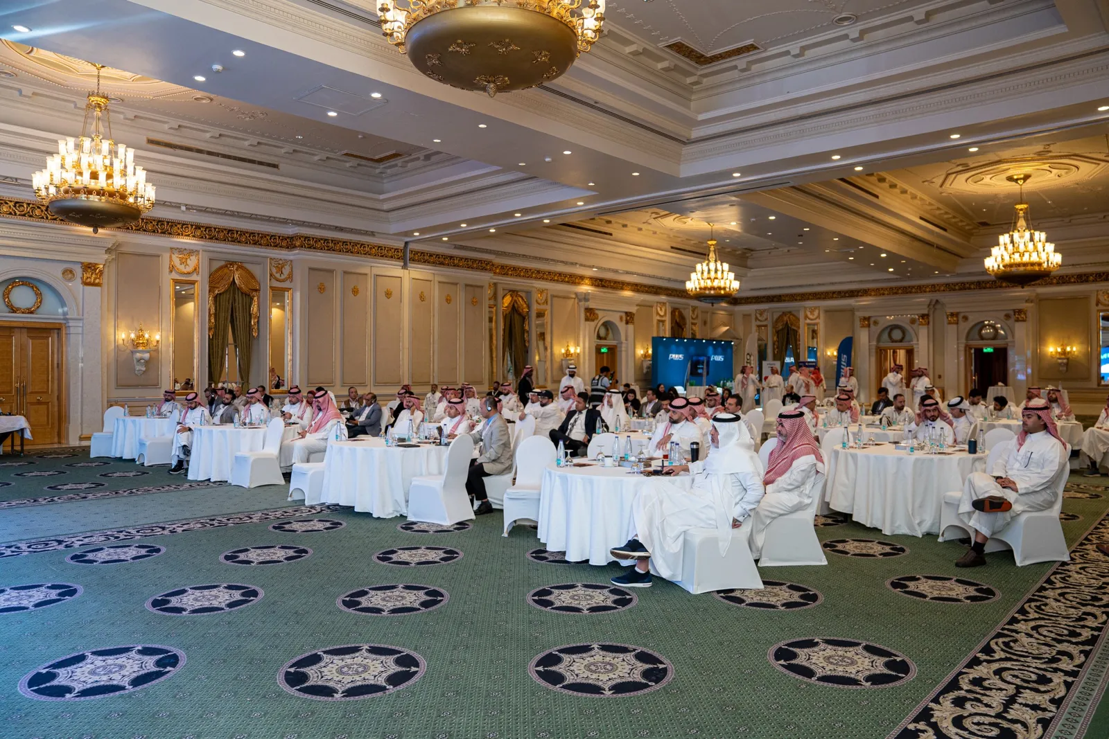 Wide ballroom full of seated guests under chandeliers